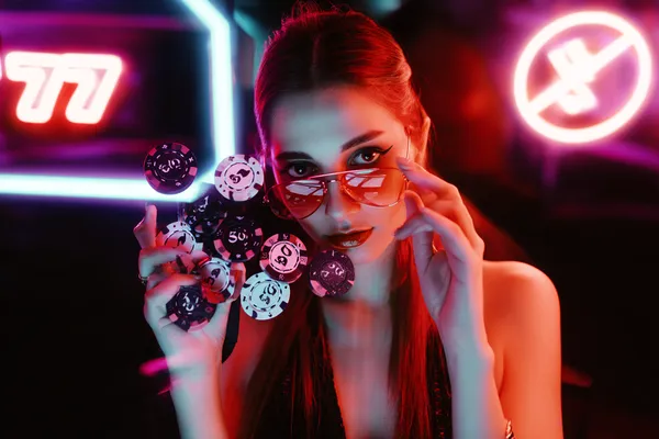 WAJA CASINO Casino — Masuk ke dalam pengalaman kasino kelas tinggi Seorang wanita glamor memegang cip kasino dalam suasana neon, mewakili pengalaman kasino dalam talian premium WAJA CASINO.